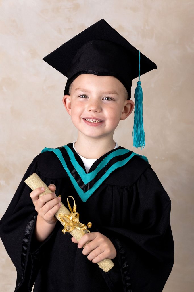 Grade R graduation photo with scroll and hat, indoor studio photo with a light background