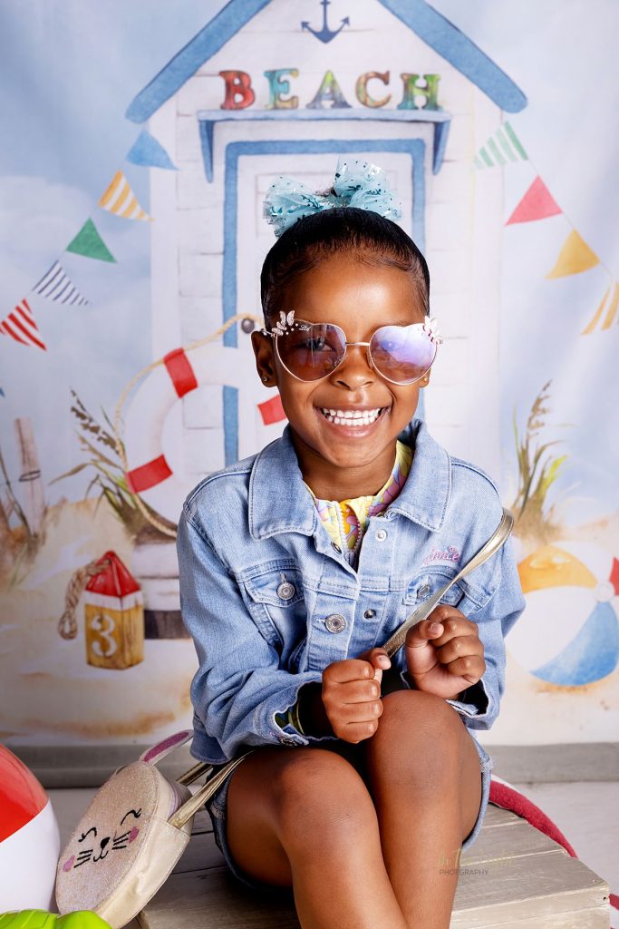 Nursery school photo of a girl smiling with a beach themed studio backdrop in Midstream