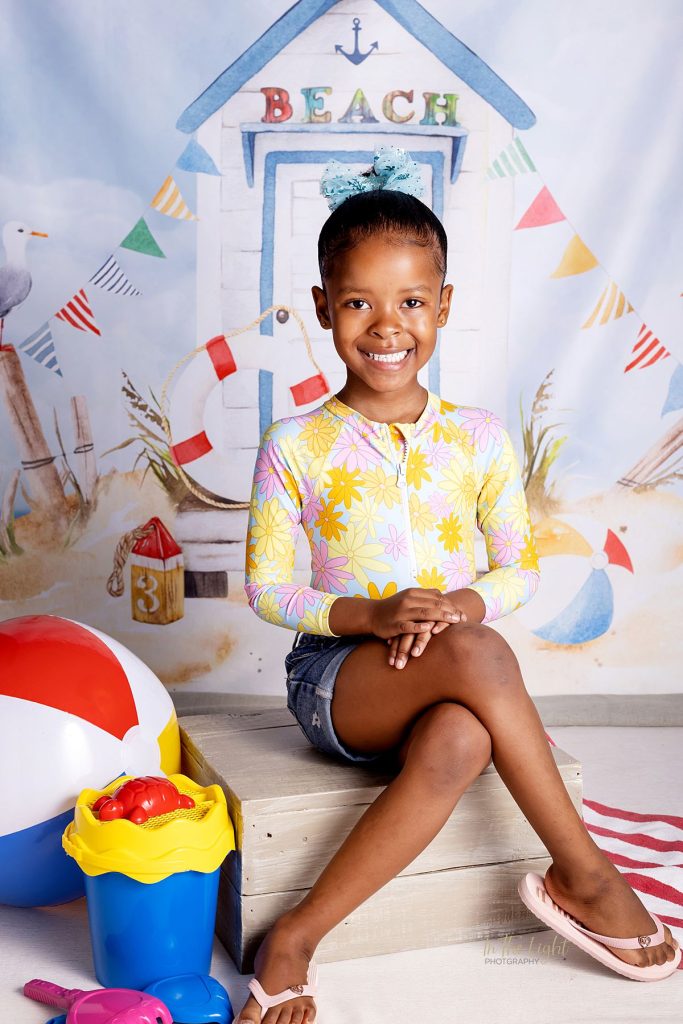 Nursery school photo of a girl smiling with a beach themed studio backdrop in Midstream
