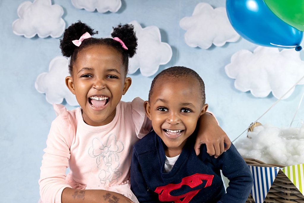 Preschool portrait photo of siblings laughing with a blue cloud backdrop, in Pretoria east